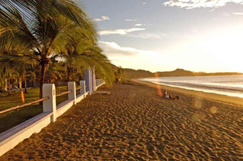 Playa Potrero at golden hour: palms along the beachfront wall and the long curve of sand round the bay, near Playa Flamingo, Costa Rica